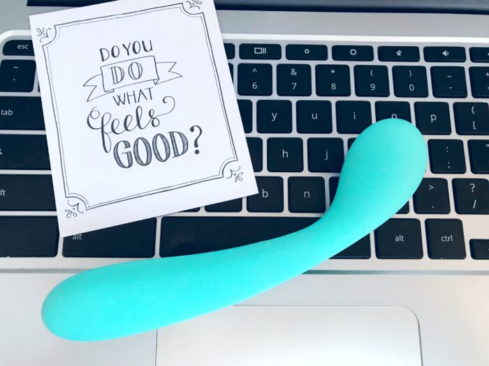 small curved dildo in aqua green/blue sitting on a laptop keyboard
