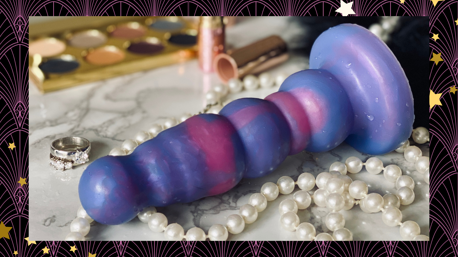 a pink and purple dildo on a marble tabletop. int he background are pearls, makeup, etc.